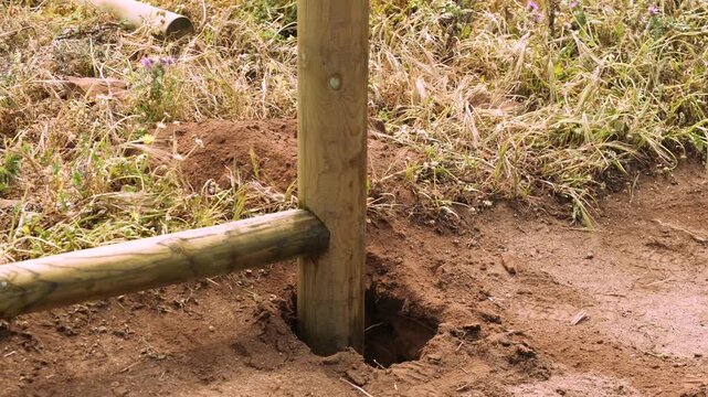 Worker diligently sets fence post in rural outdoor environment