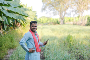 Fototapeta premium young indian farmer using smartphone standing at agricultural field