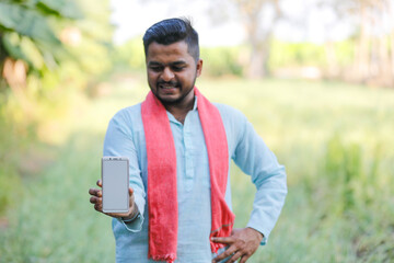 Fototapeta premium young indian farmer showing smartphone screen sitting at green agricultural field