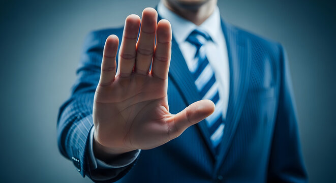Stop Gesture: A businessman in a crisp blue suit and tie holds up his hand in a clear stop gesture, conveying a message of refusal or caution against a muted blue background.