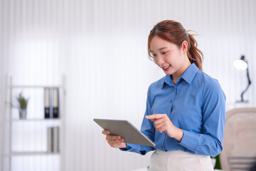 young Asian business woman professional employee using digital tablet computer browsing online working standing office modern workplace corporate environment © Pichsakul