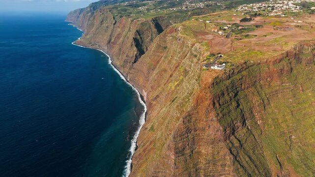 Rugged Atlantic coastline of Madeira Island with Ponta do Pargo lighthouse perched on high cliffs, drone shot