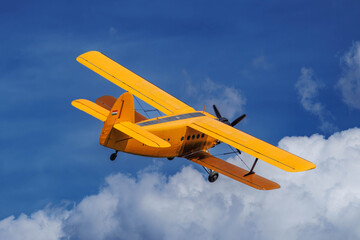 Vintage yellow Antonov An-2 biplane climbing in flight against deep blue sky and white cumulus clouds © Tams