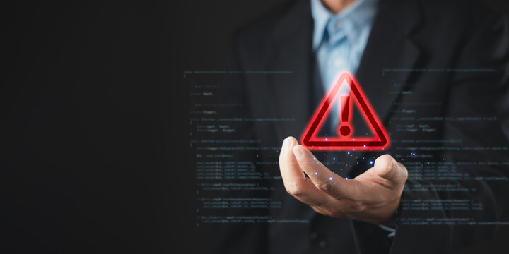 Businessman holding glowing red warning triangle icon with computer code background, cyber security and system error concept