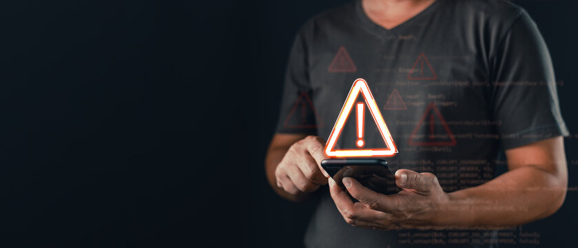 Man holding smartphone with glowing warning triangle icon and computer code overlay, cybersecurity alert and system error concept