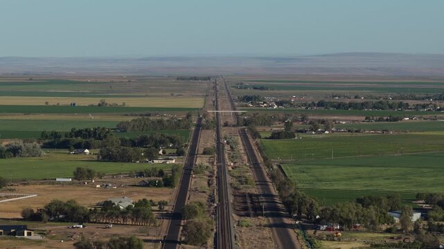 Aerial of train tracks through Mountain Home Idaho flat agricultural land at sunset with green pastures