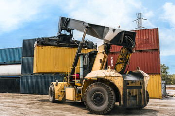 Obraz premium Loaded container handler forklift moving cargo container in crowded shipping yard at port terminal