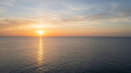 Obraz premium Serene ocean sunset with golden sun and calm water.