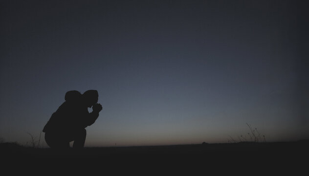 Silhouette of a man against the background of a blue sky and sunset. A man is kneeling and praying. Prayer to God. Evening