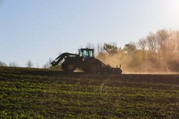 Fototapeta premium Backlit silhouette of unrecognizable man plowing field in heavy-duty agricultural machine raising dust, St-Augustin-de-Desmaures, Quebec, Canada