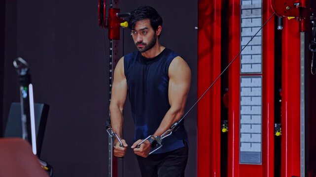 Fit man performing chest exercise on red cable crossover machine during intense dark gym workout session showing deep focus determination building heavy muscle strength for healthy physical lifestyle