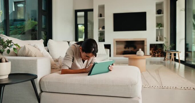 Woman, laughing and chill with tablet in home, scroll or reading ebook and thinking with non fiction. Browse, novel and mature person with tech for entertainment, remember or relax with smile on sofa