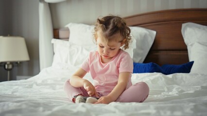 Fototapeta premium Toddler girl sitting cross legged on a comfortable bed, engaged with a mobile device, representing early childhood technology use, learning, and home based entertainment