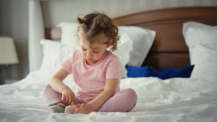 Fototapeta premium Little girl in pajamas sitting on a cozy bed, absorbed in a smartphone app, portraying childhood screen time, learning and playful digital exploration at home