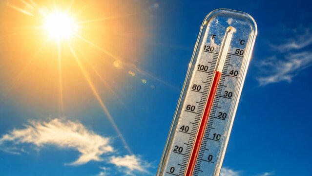 A thermometer displays high temperatures under a bright sun against a clear blue sky, indicating warm weather.