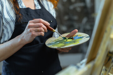 Obraz premium Female artist holding paintbrush and palette indoors