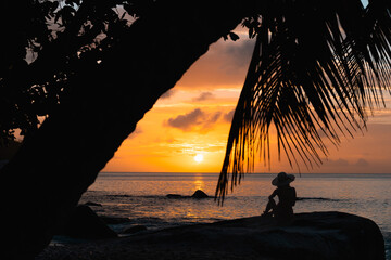 Silhouette of woman sitting on granite boulder at sunset, Anse Lazio Beach, Seychelles © Maurizio De Mattei