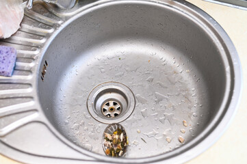 Obraz premium sink with food scraps near drain, sink surface covered with water drops and debris, metal basin in kitchen, hygiene problem concept, household cleaning, closeup detail, domestic background
