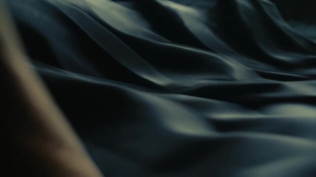 Dark silky fabric with soft flowing folds captured in realistic style on dim background, concept of elegance and texture