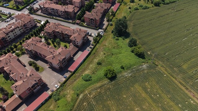 Aerial View of Urban Expansion: A modern residential area with terracotta-roofed buildings stands adjacent to a vibrant green agricultural field. Tribiano, Milan, Italy,