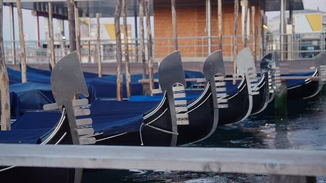 Close-up of traditional Venetian gondolas moored on calm morning water. Decorative metal ferro gently moves with soft waves, classic Venice culture and canal transportation.