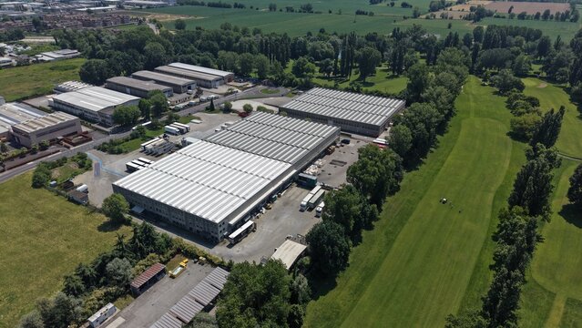 Industrial Park Aerial View: An aerial view showcases a modern industrial park featuring large factory buildings with solar panels, surrounded by lush green trees and fields.