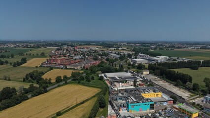 Obraz premium Aerial View of Industrial Park and Farmland: A sprawling industrial park with modern buildings and warehouses sits adjacent to golden fields of harvested crops, under a clear blue sky.