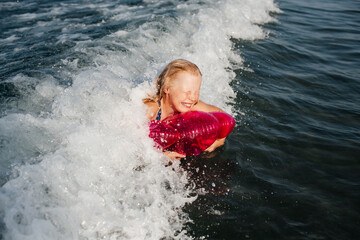 Fototapeta premium Laughing teenage girl riding breaking wave on pink inflatable ring