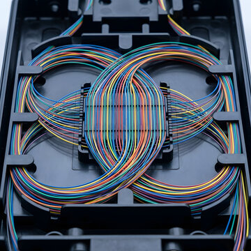 Open fiber optic splice enclosure with colorful looped optical fibers in organized routing pattern. Telecommunications, broadband infrastructure and high speed internet network concept.