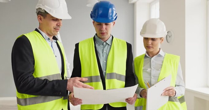 Construction workers and engineers planning blueprint inspection. Architects guide teamwork with helmets indoors. They review renovation plans. Teamwork delivers safe project outcomes on time.