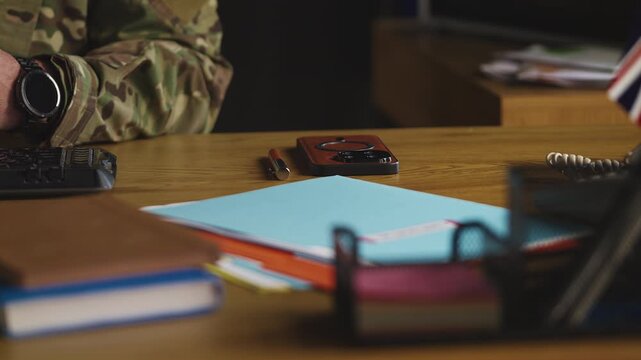 U.K. army general typing on computer in command center, controlling mission
