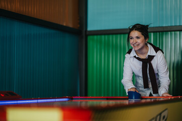 A smiling woman and her friend play air hockey at a colorful arcade table. The friends laugh and...