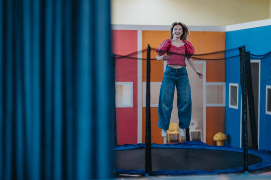 Two friends leap together on an indoor trampoline, smiling and captured midair. The playful scene shows energetic movement and bright, colorful surroundings.
