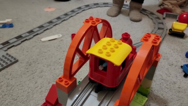 Toy plastic train moving on tracks before an orange bridge toy