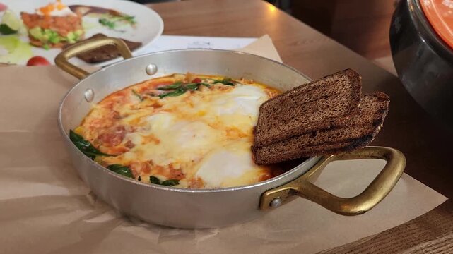 Shakshuka with fried eggs and dark rye bread served in a metal frying pan