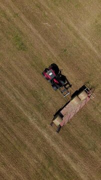 Harvesting Hay Bales: An aerial view captures a tractor pulling a trailer loaded with hay bales across a vast, mowed field, illustrating agricultural labor.