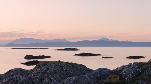 Pale pink sunset over misty mountains and ripples in calm sea on west coast of Scotland looking towards Skye