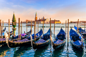 row of parked venetian gondola boats in Grand canal of Venice. Beautiful sunset or sunrise landscape with gondolas in blue water of Venice. © Yaroslav