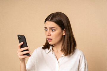 Naklejka premium Young woman reacts with shock and disbelief to something on her smartphone screen