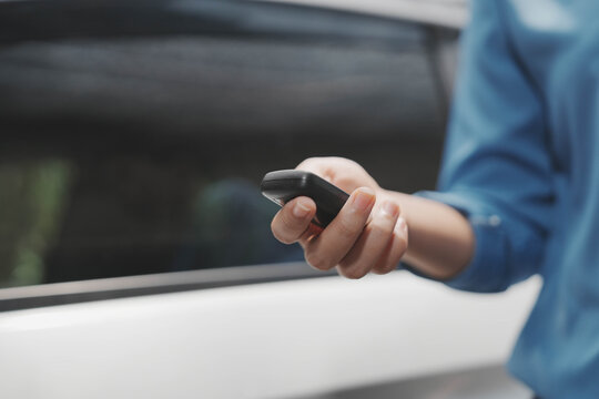 Close-up of a person holding a car key fob near a vehicle door, suggesting remote locking or unlocking, modern transportation and security concept.
