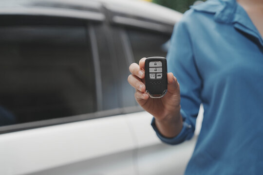 Close-up of person holding car key fob near a white vehicle, concept of buying, renting, or unlocking a modern car with remote entry.