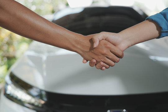 Two people shaking hands in front of a car, suggesting a successful vehicle purchase or service agreement at a dealership or garage.