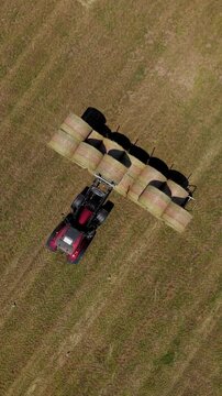 Tractor Transporting Hay Bales: An aerial view captures a red tractor hauling a long line of round hay bales across a dry, cut field, showcasing agricultural work.