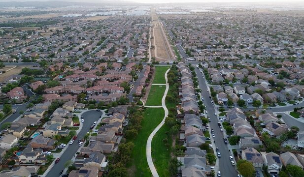 Aerial view of suburban neighborhood and residential housing development with central greenbelt park, walking path, and streets in Perris California