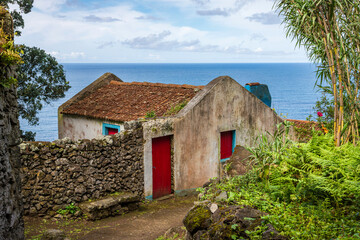 Traditional lava stone cottage with a red door along the Rocha da Relva hiking trail in Sao Miguel Island, Azores, Portugal. The rustic building sits near the Atlantic Ocean. © Max Maximov