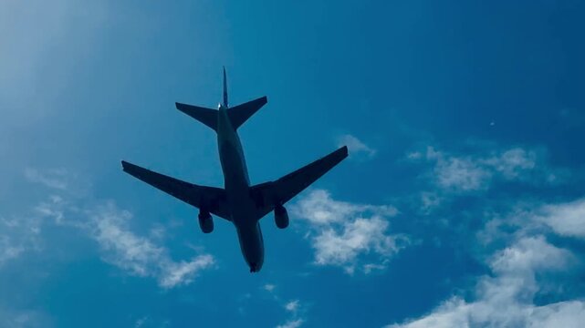 Low angle view of passenger jetliner cabin fuselage, metal wings and tail section flying in sky. Commercial aircraft jet engine propulsion and wing flaps on background of white clouds.