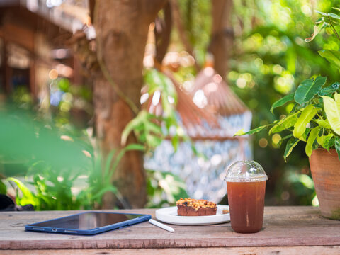 Remote Work Setup with Iced Coffee, Cake, and Tablet in Shady Garden