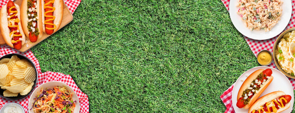 Summer outdoor BBQ double border with hot dogs, classic salads and snacks. Top down view over a red and white check cloth and grass banner background.