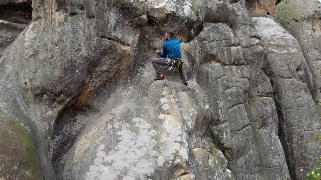Drone shot of athlete moving up rugged cliff with chalked holds and protective equipment. Extreme sport footage for performance, courage, balance, and wilderness recreation themes