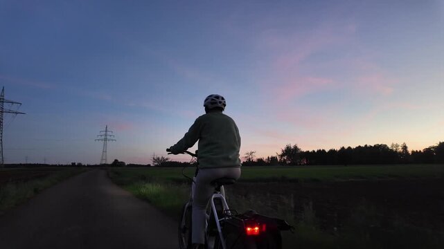Woman cyclist riding electric bicycle on rural road in evening countryside  